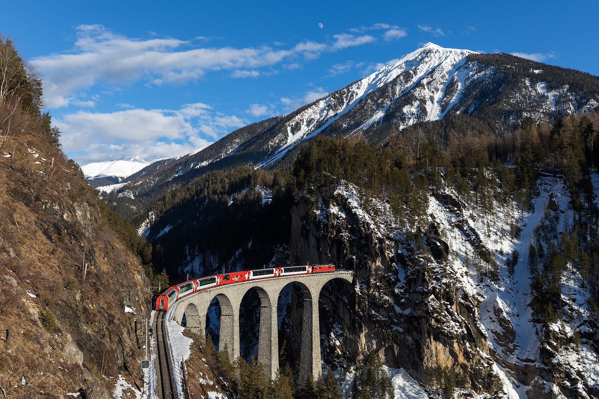 A red train crossing the Landwasser Viaduct in the Alps.