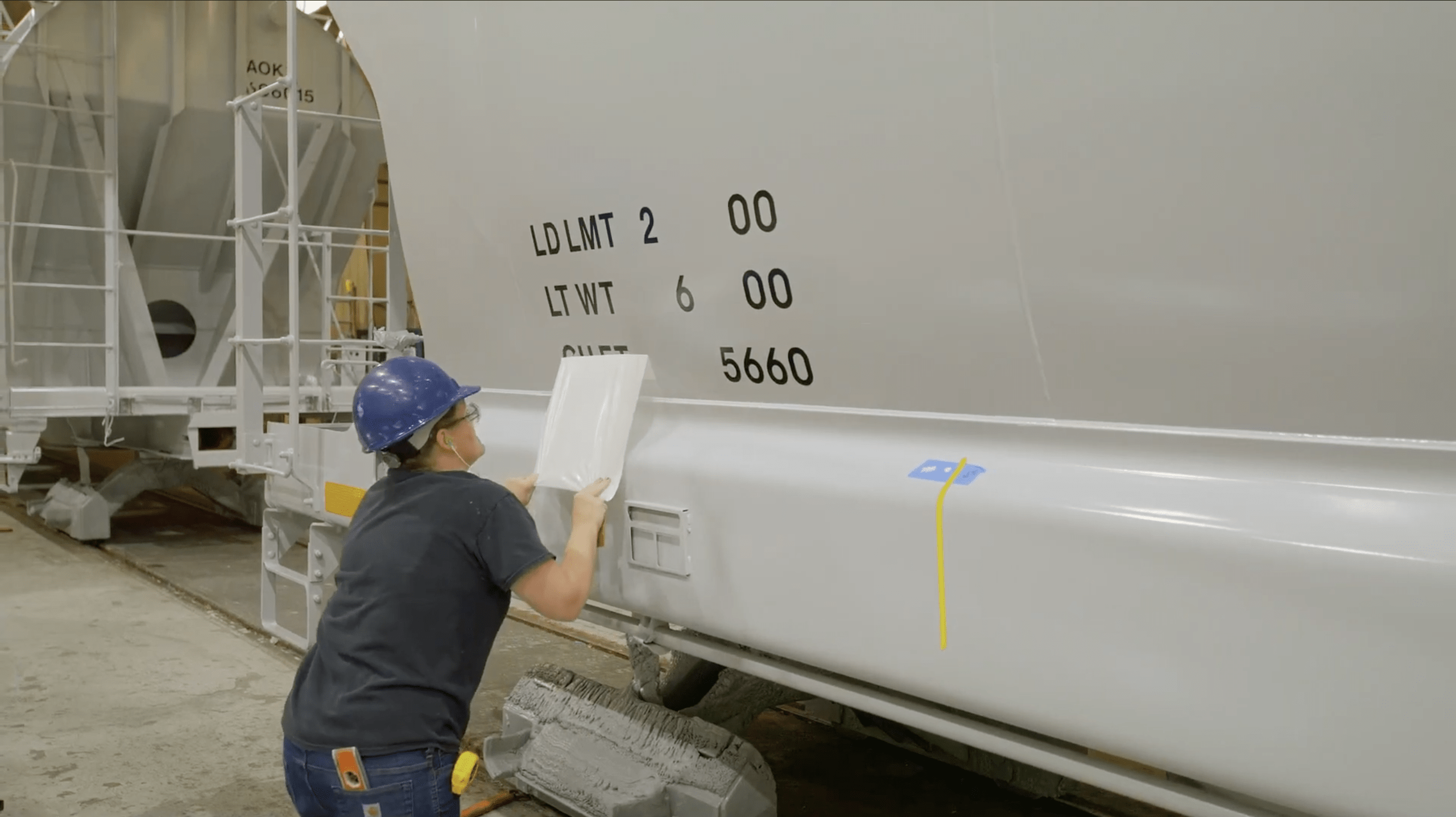A worker placing letter on the side of a white hopper railcar